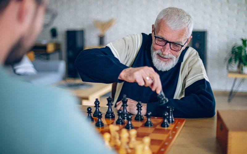 Smiling senior man playing chess with a volunteer in the living room