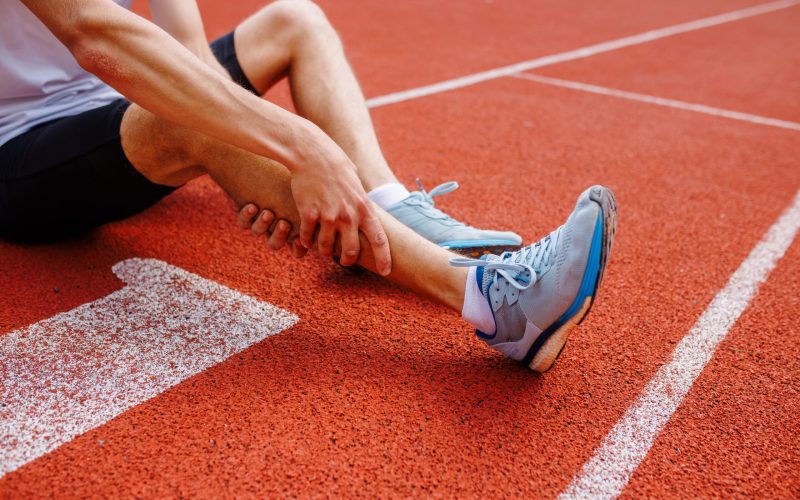 Athlete holding his leg injured after running at track and field stadium after jogging, running competition, sports injury concept